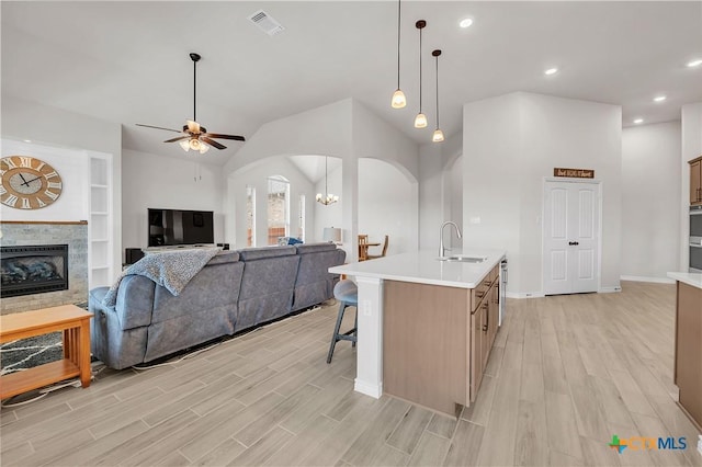 kitchen featuring a stone fireplace, sink, hanging light fixtures, a center island with sink, and ceiling fan