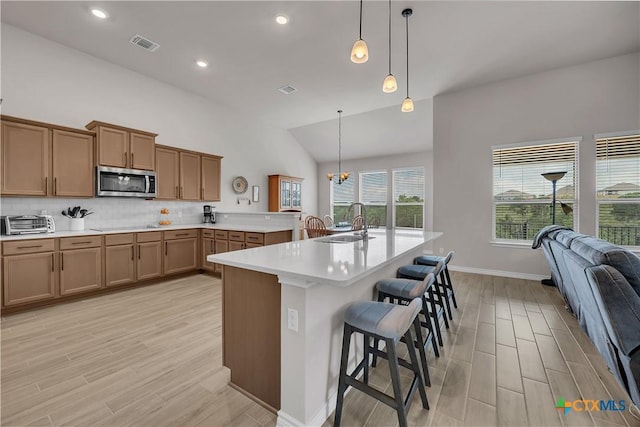 kitchen featuring decorative light fixtures, tasteful backsplash, sink, a breakfast bar area, and light hardwood / wood-style floors