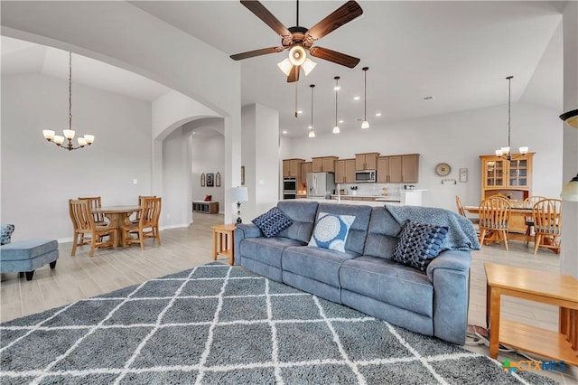 living room featuring high vaulted ceiling, ceiling fan with notable chandelier, and light hardwood / wood-style floors