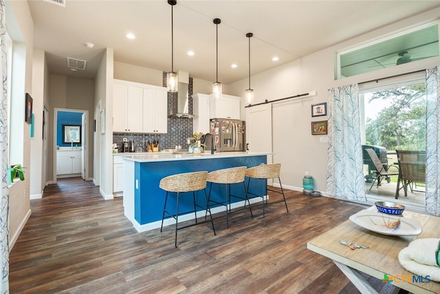 kitchen featuring a center island with sink, stainless steel fridge, decorative light fixtures, a barn door, and white cabinets