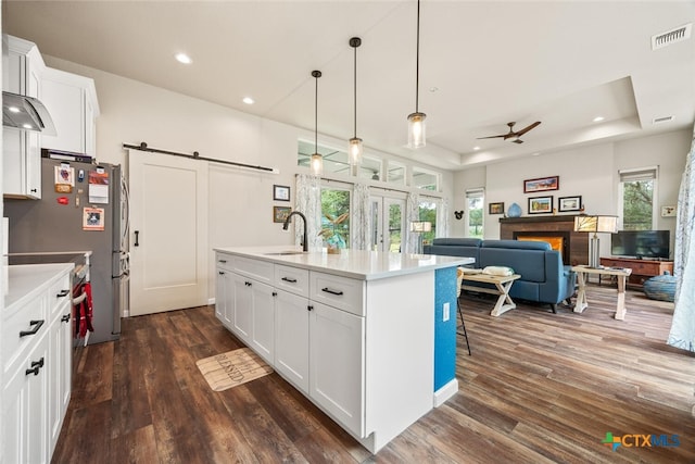 kitchen featuring dark wood-type flooring, a center island with sink, white cabinets, a barn door, and ceiling fan