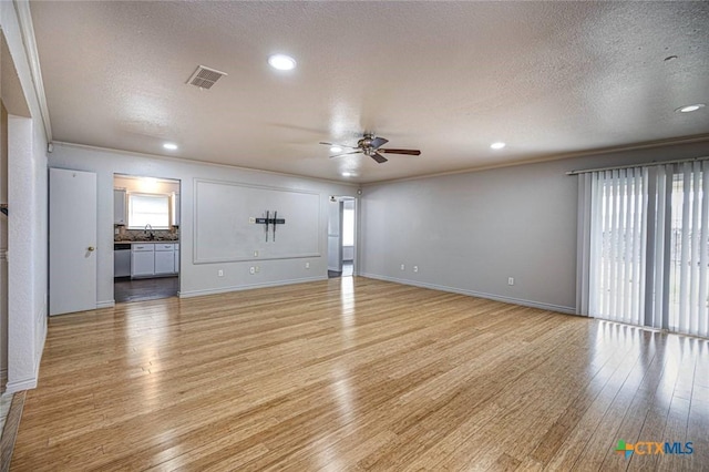 unfurnished living room featuring ceiling fan, ornamental molding, a textured ceiling, and light wood-type flooring