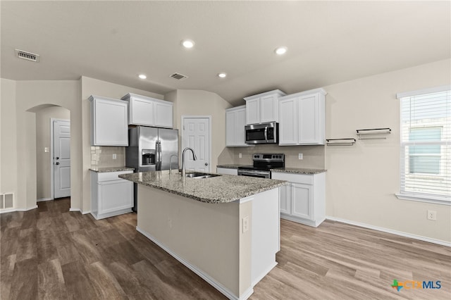 2503 Pintail Loop, Copperas Cove, TX 76522 - kitchen featuring appliances with stainless steel finishes, arched walkways, light wood-style flooring, backsplash, and an island with sink