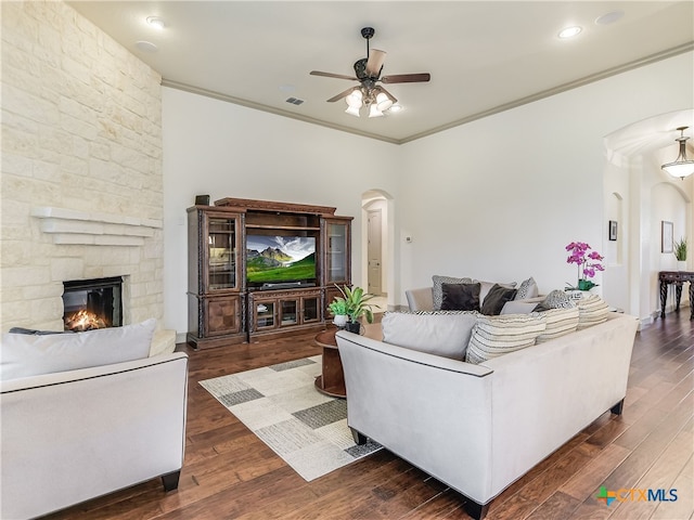 535 Mission Hill Run, New Braunfels, TX 78132 - living room featuring arched walkways, ceiling fan, crown molding, a stone fireplace, and dark wood finished floors