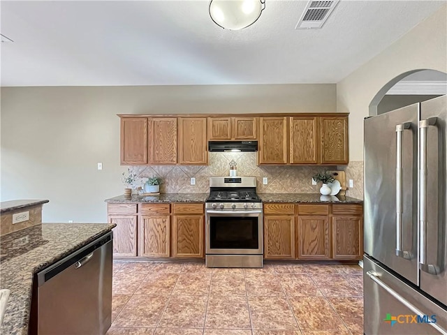 kitchen featuring tasteful backsplash, extractor fan, appliances with stainless steel finishes, and dark stone countertops