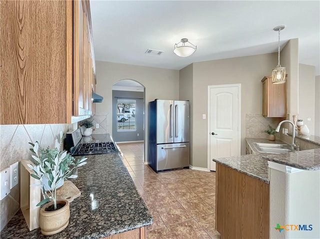 kitchen featuring tasteful backsplash, sink, stainless steel fridge, hanging light fixtures, and stove