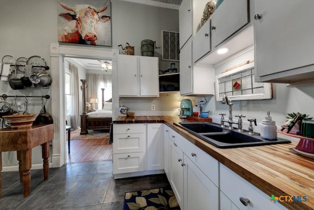 kitchen featuring open shelves, wooden counters, white cabinets, and a sink