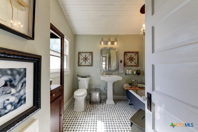 full bathroom featuring a soaking tub, toilet, baseboards, and vaulted ceiling