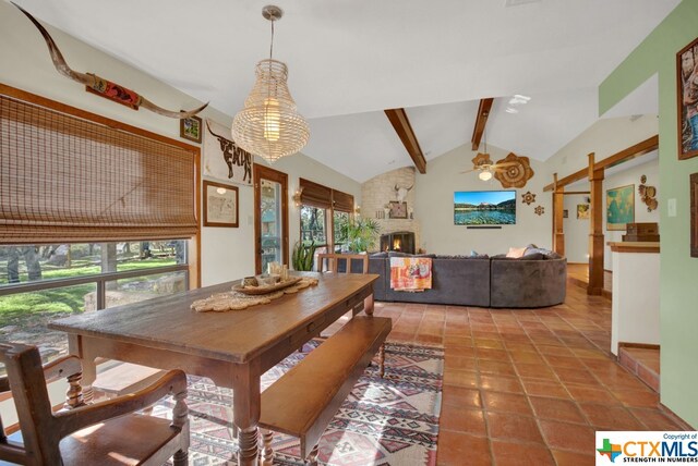 tiled dining room with a stone fireplace, lofted ceiling with beams, and ceiling fan