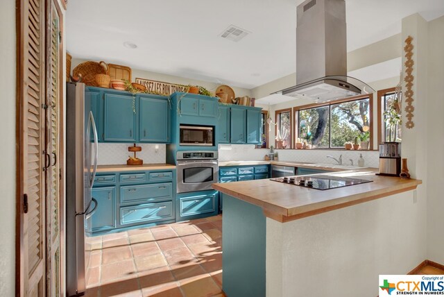 kitchen with blue cabinets, kitchen peninsula, light tile patterned floors, island exhaust hood, and appliances with stainless steel finishes