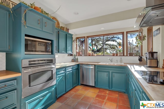 kitchen featuring stainless steel appliances, ventilation hood, backsplash, and blue cabinetry