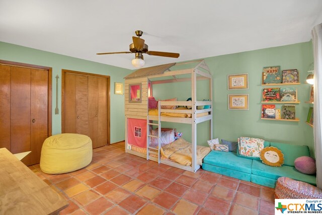 tiled bedroom with ceiling fan and two closets