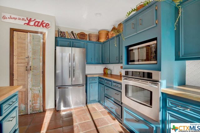 kitchen featuring stainless steel appliances, blue cabinetry, light tile patterned floors, and decorative backsplash