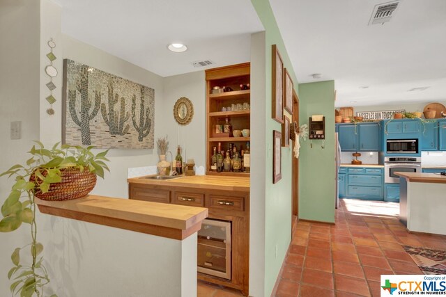 bar with beverage cooler, blue cabinets, sink, wood counters, and appliances with stainless steel finishes