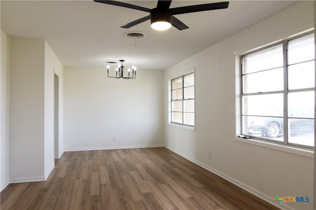 empty room with ceiling fan with notable chandelier, wood finished floors, visible vents, and baseboards