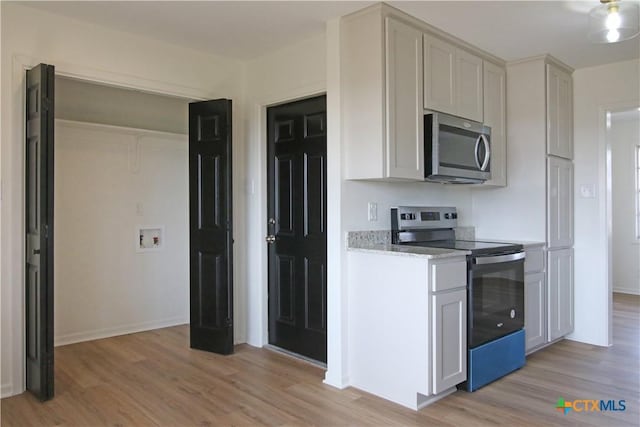 kitchen with light stone countertops, light wood-style floors, baseboards, and appliances with stainless steel finishes