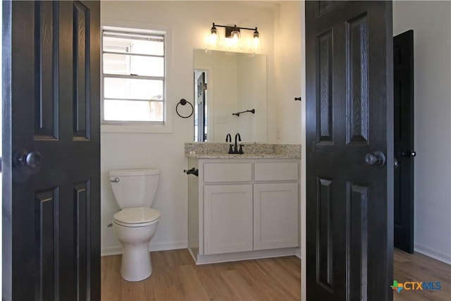 bathroom with baseboards, toilet, wood finished floors, and vanity