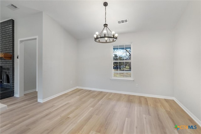 unfurnished dining area featuring light wood-type flooring, a brick fireplace, and a notable chandelier