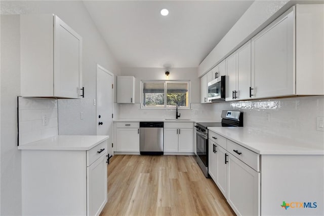 kitchen with light hardwood / wood-style floors, stainless steel appliances, backsplash, white cabinets, and sink