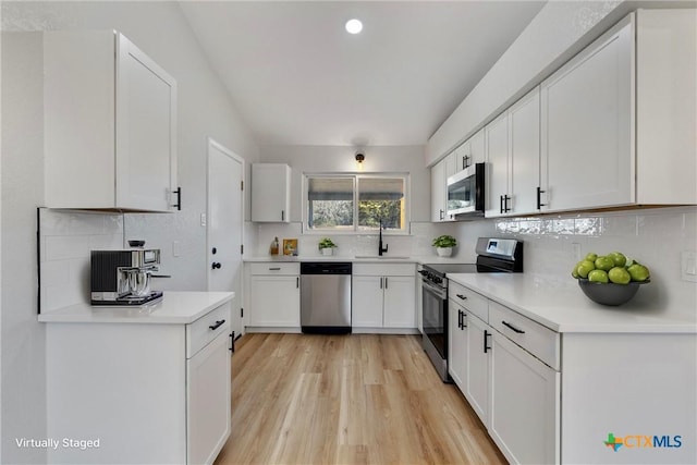 kitchen featuring appliances with stainless steel finishes, white cabinetry, sink, backsplash, and light wood-type flooring