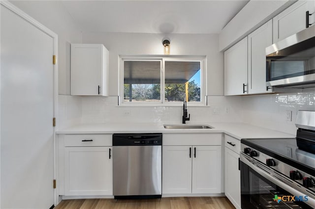 kitchen with white cabinets, appliances with stainless steel finishes, sink, backsplash, and light wood-type flooring