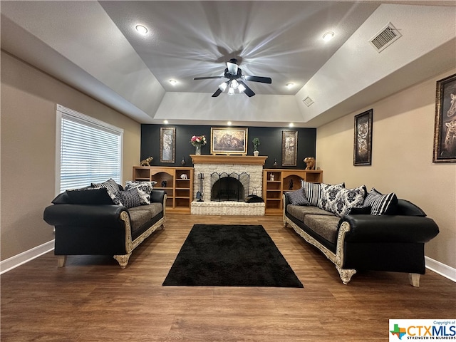 living room with hardwood / wood-style floors, a raised ceiling, ceiling fan, and a stone fireplace