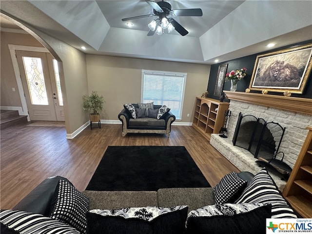 living room with a tray ceiling, ceiling fan, hardwood / wood-style floors, a stone fireplace, and lofted ceiling