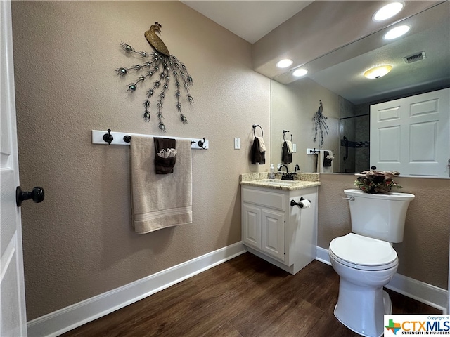 bathroom with a tile shower, hardwood / wood-style floors, vanity, and toilet