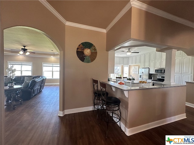 kitchen with kitchen peninsula, a kitchen breakfast bar, dark hardwood / wood-style flooring, stainless steel appliances, and white cabinetry