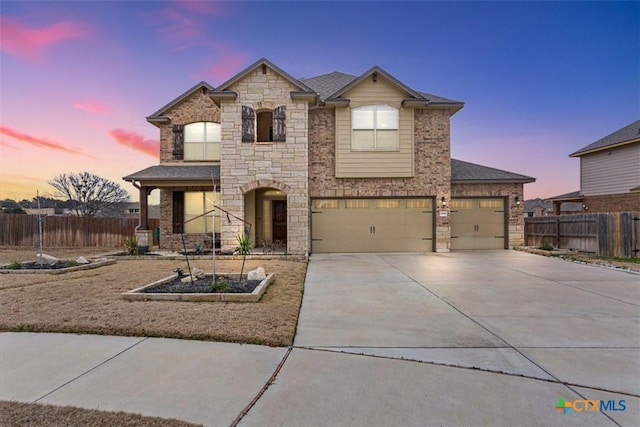 view of front of home with a shingled roof, concrete driveway, an attached garage, fence, and stone siding