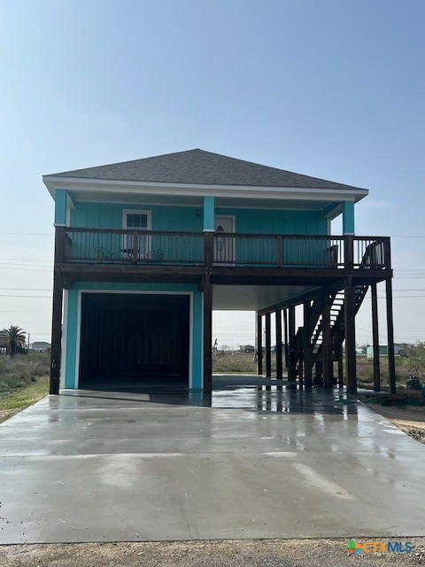 raised beach house with an attached garage, a carport, and concrete driveway