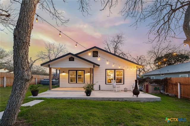 back of house at dusk with a patio area, a lawn, and a fenced backyard