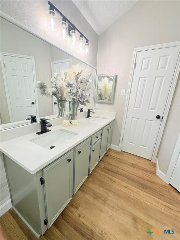 421 Arapaho Dr, Harker Heights, TX 76548 - bathroom with double vanity, wood finished floors, a textured ceiling, baseboards, and vaulted ceiling