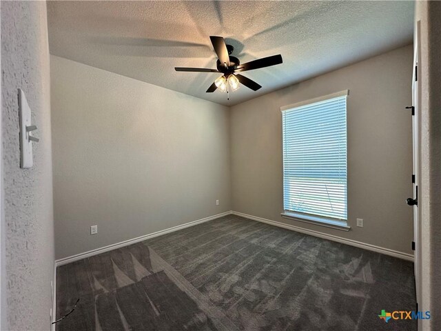 empty room with dark carpet, ceiling fan, a textured ceiling, and baseboards
