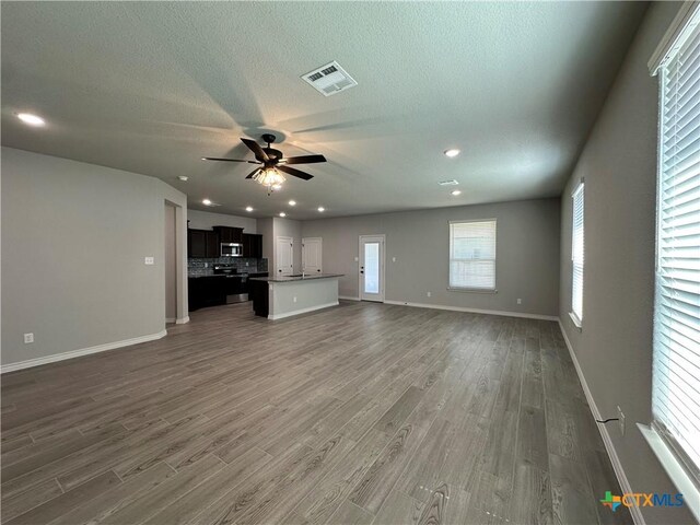 unfurnished living room with ceiling fan, wood finished floors, baseboards, a textured ceiling, and recessed lighting
