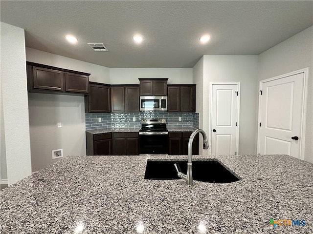 kitchen with stainless steel appliances, dark stone counters, decorative backsplash, dark brown cabinets, and recessed lighting