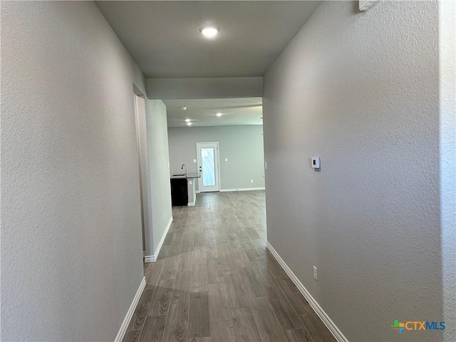 hall with baseboards, dark wood-style flooring, a textured wall, and a sink
