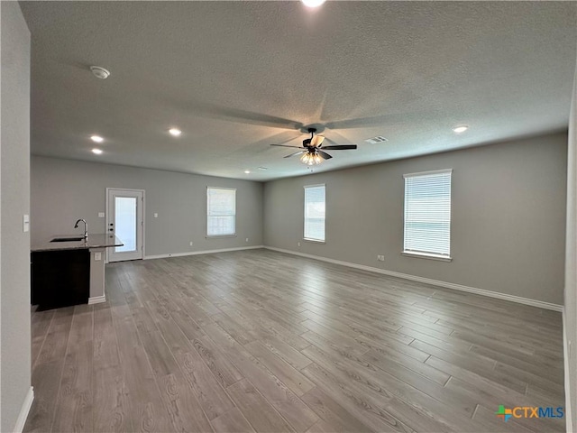 unfurnished living room with a ceiling fan, a textured ceiling, baseboards, light wood-type flooring, and a sink