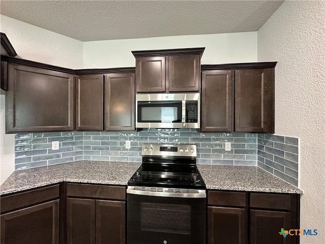 kitchen with appliances with stainless steel finishes, dark brown cabinets, decorative backsplash, light stone countertops, and a textured wall