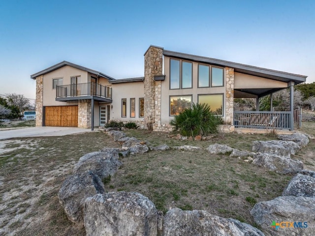 view of front facade featuring an attached garage, a balcony, stone siding, concrete driveway, and stucco siding