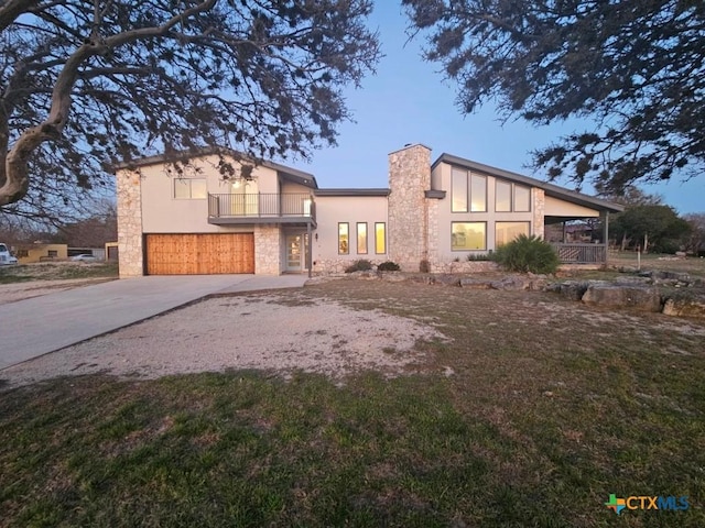 view of front of property with a chimney, stucco siding, concrete driveway, a balcony, and stone siding