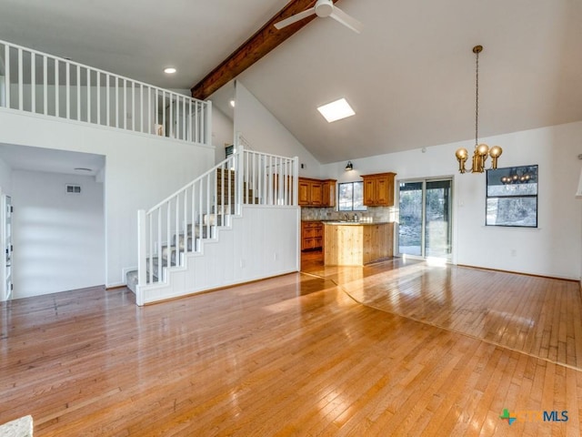 unfurnished living room featuring visible vents, light wood-style flooring, stairs, high vaulted ceiling, and beam ceiling