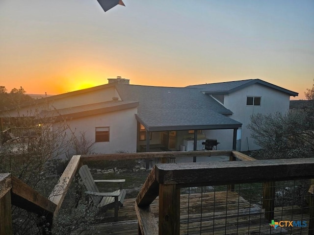 back of house at dusk featuring roof with shingles