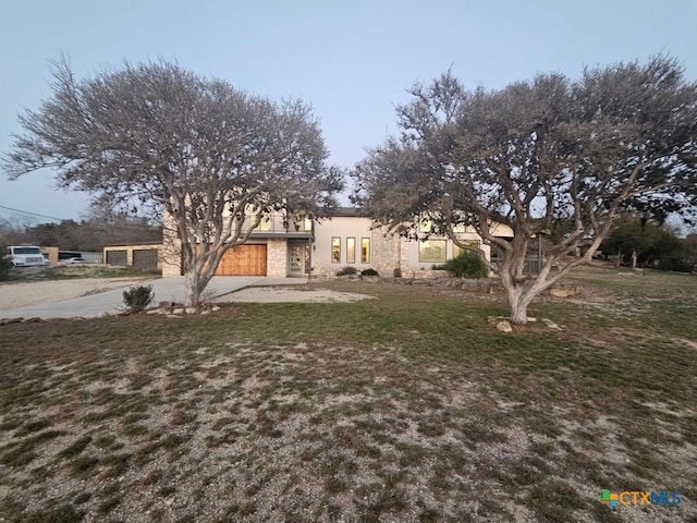 view of front of property featuring a garage, driveway, stone siding, stucco siding, and a front lawn