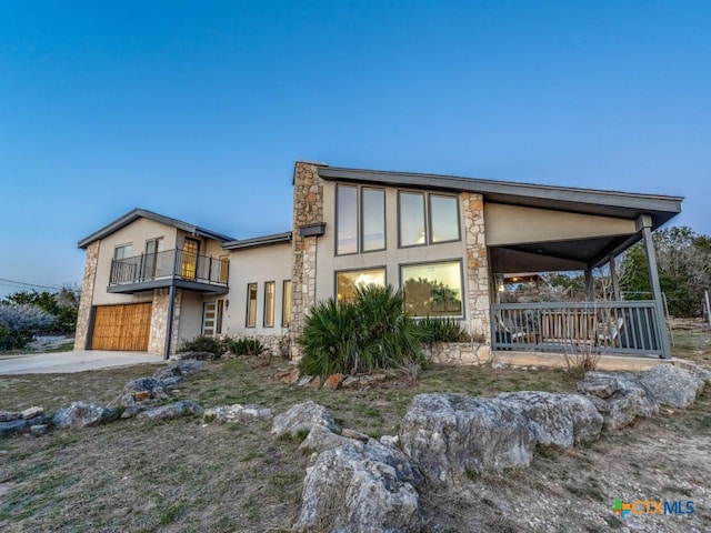 view of front of home with stucco siding, a porch, an attached garage, a balcony, and stone siding