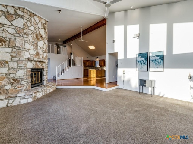 unfurnished living room featuring a ceiling fan, carpet, a fireplace, high vaulted ceiling, and beam ceiling