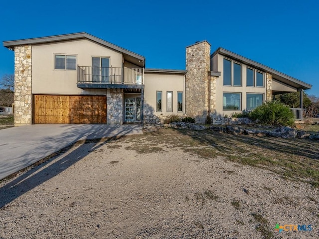 view of front of property featuring a balcony, driveway, a chimney, and stucco siding