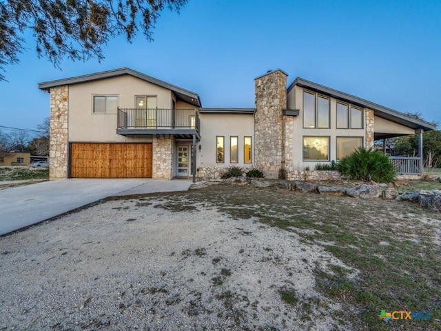 view of front of home featuring concrete driveway, a balcony, stone siding, a chimney, and stucco siding