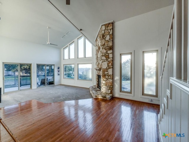 unfurnished living room featuring ceiling fan, hardwood / wood-style floors, a stone fireplace, high vaulted ceiling, and track lighting