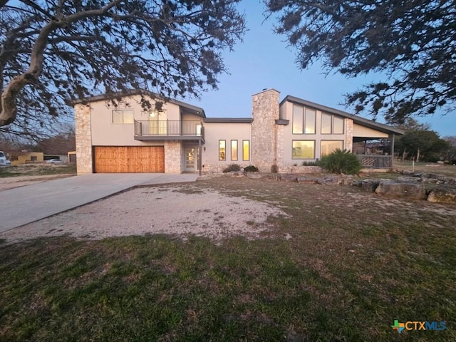 view of front of property with a chimney, stucco siding, an attached garage, a balcony, and driveway